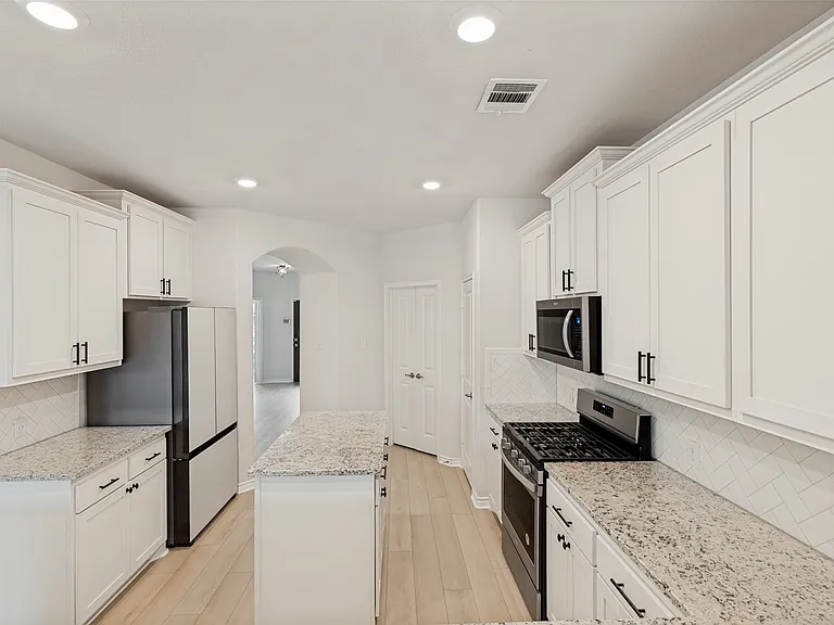 Bright kitchen featuring white shaker cabinetry with black hardware, granite countertops, a tiled backsplash, wood-finish flooring, and recessed lighting