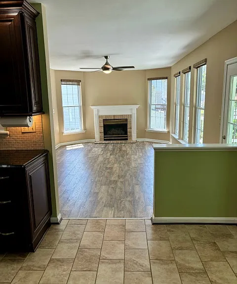 Living room with gas fireplace and ceiling fan. View from kitchen.