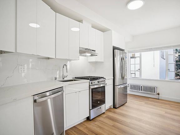 Kitchen with multiple cabinets, refrigerator, stove, range hood, and sink