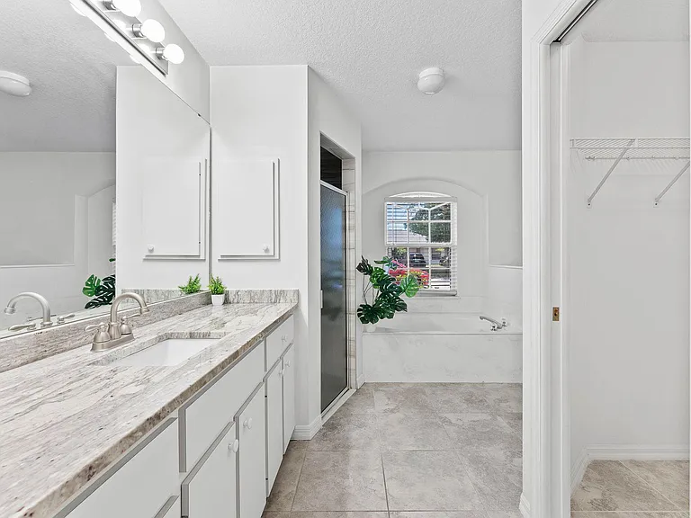 Spacious bathroom with double vanity, granite-look counters, walk-in shower, soaking tub, and a linen closet.