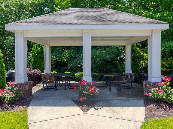 Covered outdoor pavilion with picnic tables, blooming flower beds, and lush green backdrop, ideal for socializing at Snowden Senior Apartments.