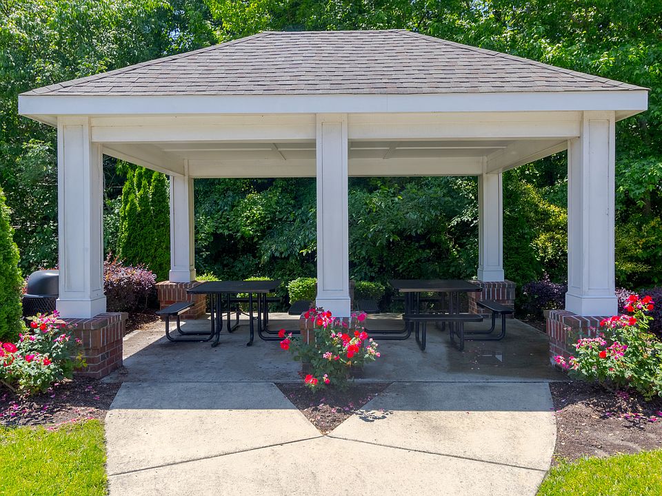 Covered outdoor pavilion with picnic tables, blooming flower beds, and lush green backdrop, ideal for socializing at Snowden Senior Apartments.