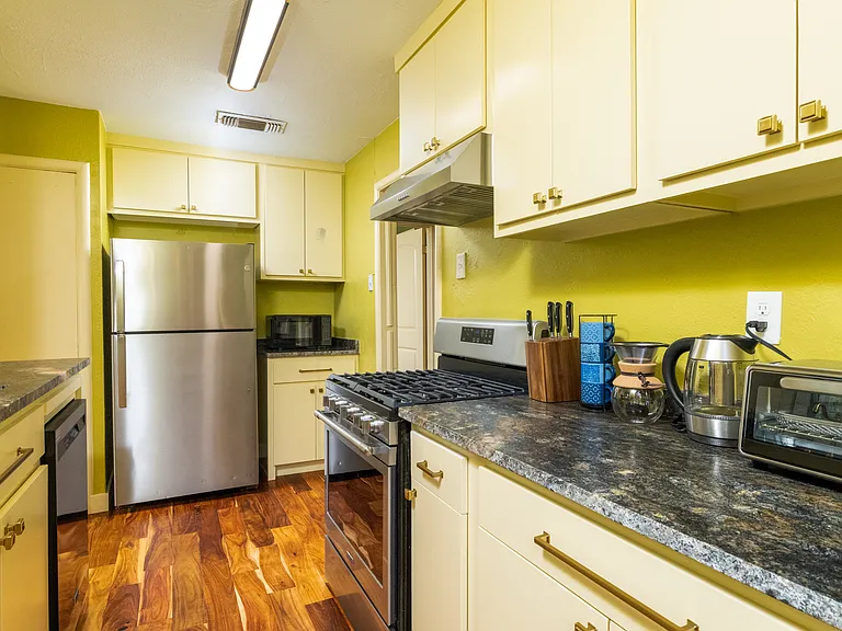 Bright, fully equipped kitchen with stainless steel appliances, warm wood floors, and modern yellow cabinets_perfect for cooking and relaxing at home.