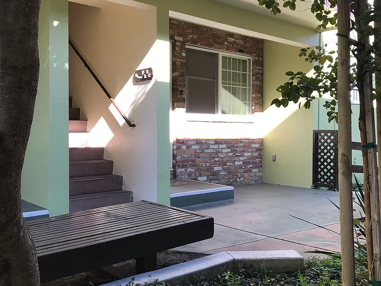 Cozy 600 square foot apartment with a front porch entry that opens to a landscaped common area and concrete walkway with wooden benches.