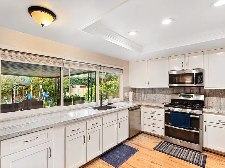 This is the white remodeled kitchen with latest design granite counters which also cover the walls. The shaker style cabinets and soft close doors and drawers is enhanced by the view of the covered patio & the beautiful green fruit trees of the backyard