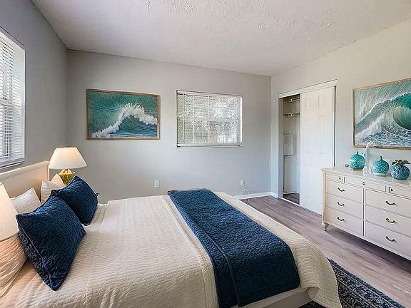 Inviting bedroom featuring elegant coastal decor, plush bedding with deep blue accents, and soft natural light streaming through large windows.