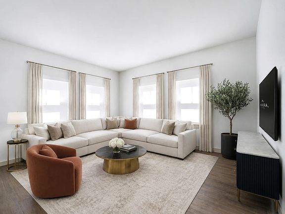 Light-filled living room with expansive corner windows, warm flooring, and ample seating designed for gathering, relaxing, and everyday comfort.