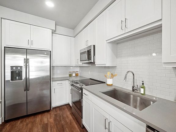 Finish Package II kitchen with stainless steel appliances, white cabinetry, white tile backsplash, and grey quartz countertops