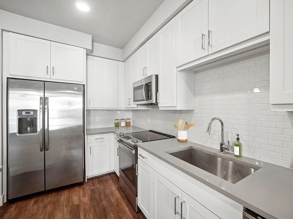 Finish Package II kitchen with stainless steel appliances, white cabinetry, white tile backsplash, and grey quartz countertops