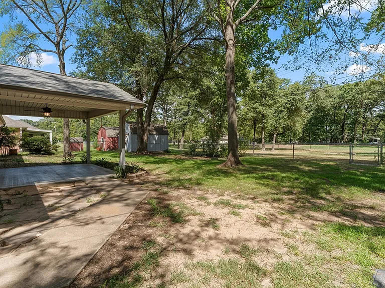 Spacious backyard featuring a covered patio, a shed, mature trees, and a chain-link fence