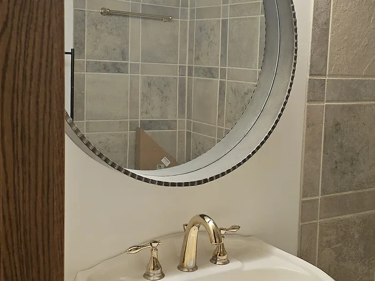 Beautiful full bathroom featuring luxurious Italian porcelain tile, a deep soaking tub with shower, and premium Kohler fixtures. The space includes a classic pedestal sink, round mirror, and elegant lighting