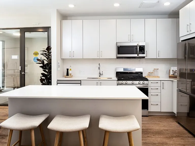 Showroom kitchen with stainless steel appliances, white quartz countertop, light grey cabinetry, and hard surface flooring