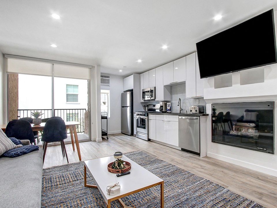 Furnished 1 Bedroom Suite, living room with cozy fireplace, dining area on the left with private balcony, open kitchen