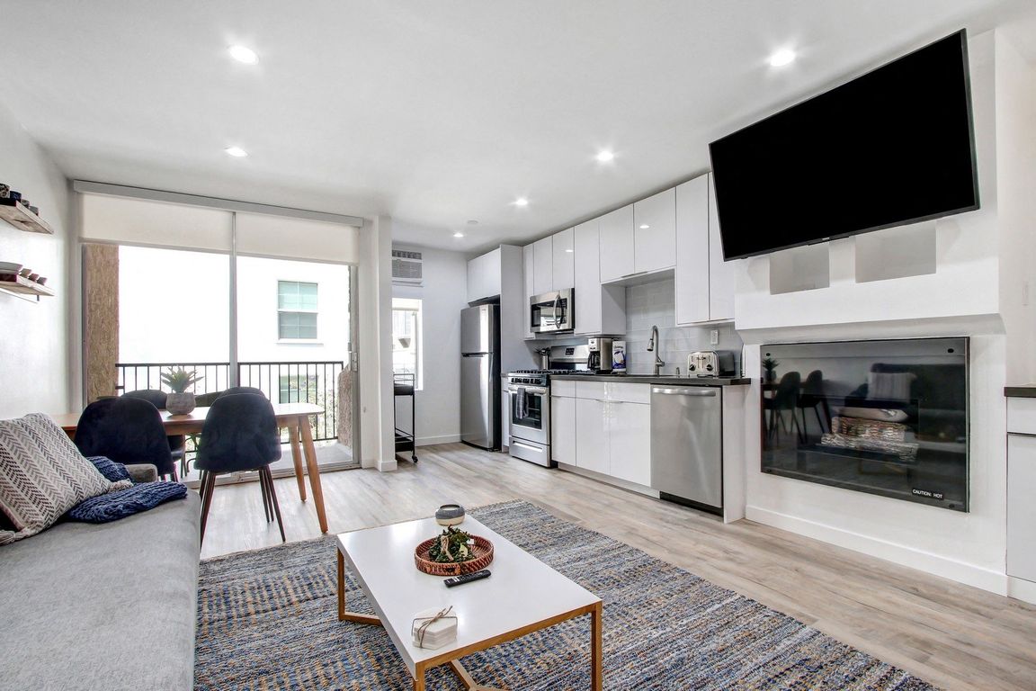 Furnished 1 Bedroom Suite, living room with cozy fireplace, dining area on the left with private balcony, open kitchen
