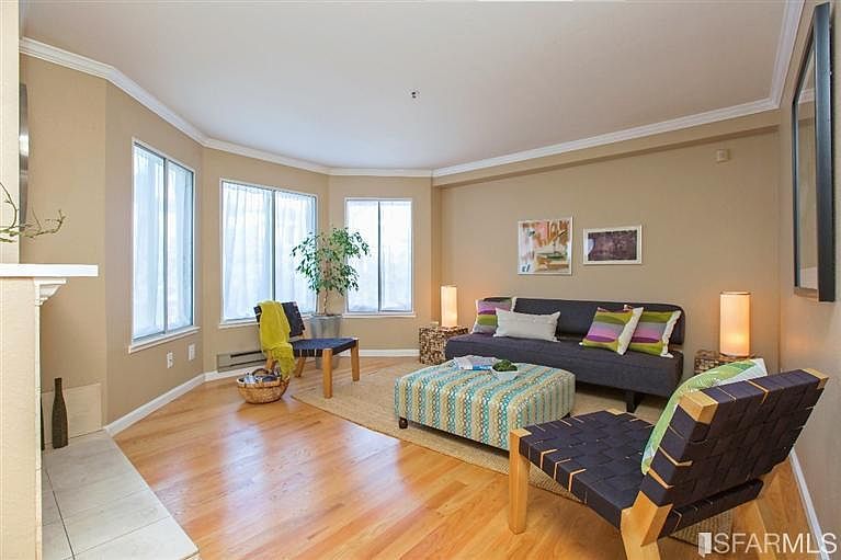 Living room with bay windows features fireplace, crown molding and hardwood floors. Furniture/photo from previous sale. Unit is vacant.