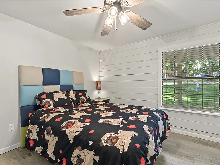 Bedroom featuring a shiplap accent wall, wood-finish flooring, and a ceiling fan with integrated lighting