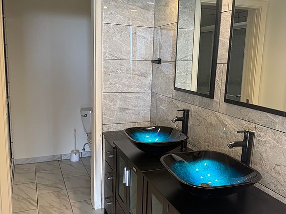 Striking primary en-suite with dual glass vessel sinks and marble tile