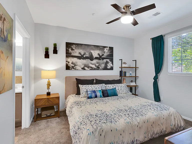 Elegant bedroom with cozy queen-sized bed, modern decor, and vibrant artwork, featuring a large window with lush green views.