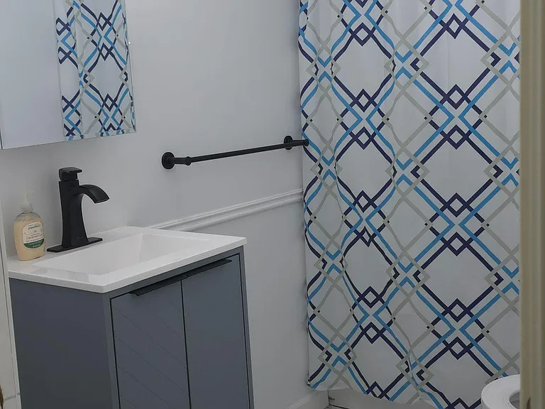 Updated bathroom featuring a sleek vanity with modern faucet, tiled shower surround, and easy-clean tile flooring.