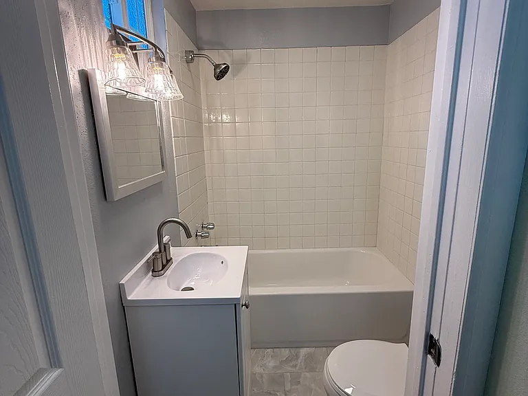 Bathroom with bathtub. New mirror, new window, new lighting fixtures, new bath fan, new toilet, new sink, new hardware, new tile flooring.