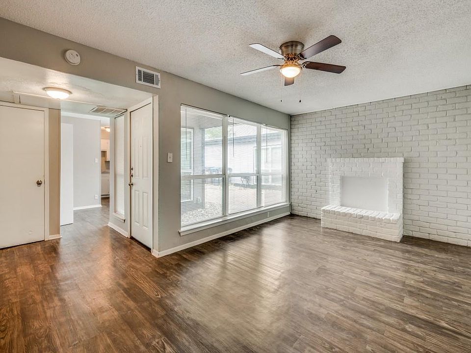 Unfurnished living room with brick wall, dark wood-style floors, a textured ceiling and a ceiling fan