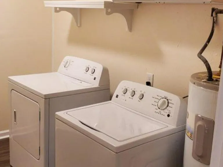 Dedicated laundry area with full-size washer and dryer, plus wall shelving for detergents and supplies.