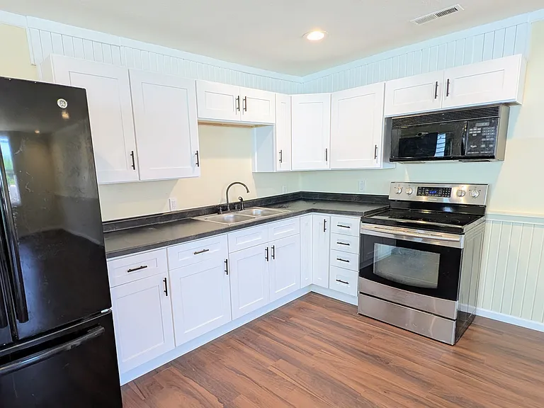 Completely updated kitchen with white shaker-style cabinets, modern black countertops, and all appliances included.