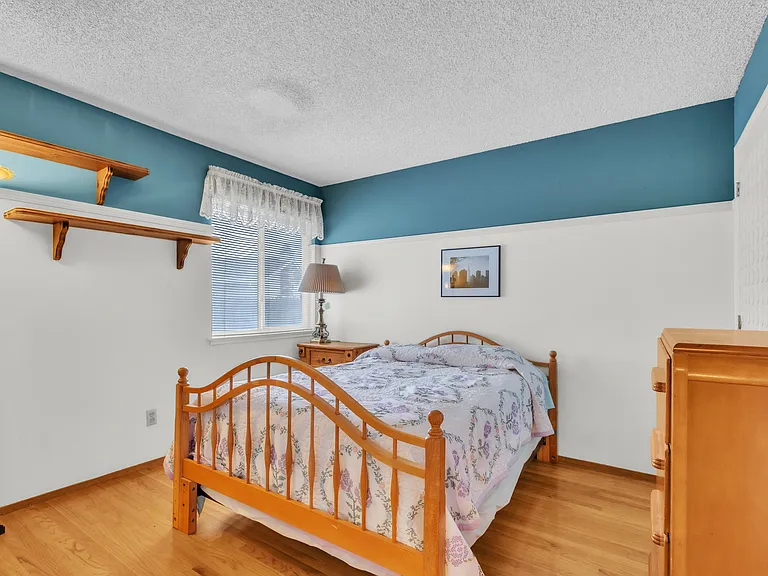 Bedroom with full-size bed, one night stand with a lamp and a standing lamp. One full dresser with one closet. Wooden floors.
