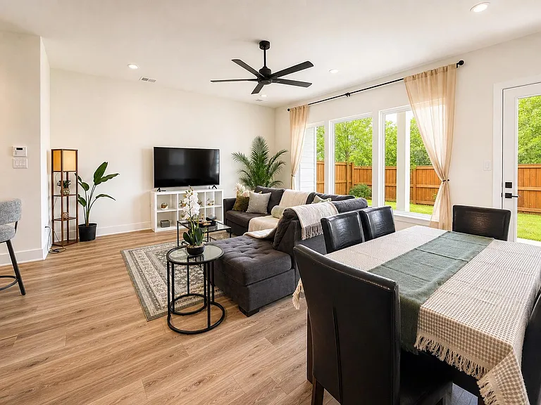 Open-concept living and dining area with ceiling fan, large windows, and sliding door access to a fenced backyard patio.