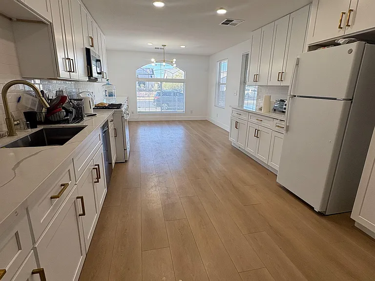 Galley-style kitchen with ample white cabinetry, full-size fridge, and generous counter space, opening to an eat-in area.