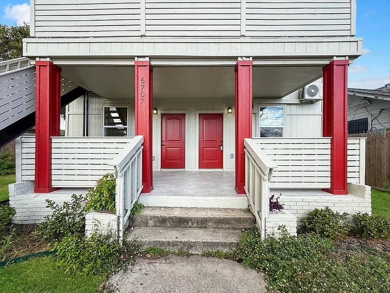 Charming entryway of a home featuring bold red doors and pillars, with a cozy covered porch and neatly maintained greenery. Ideal for welcoming guests.