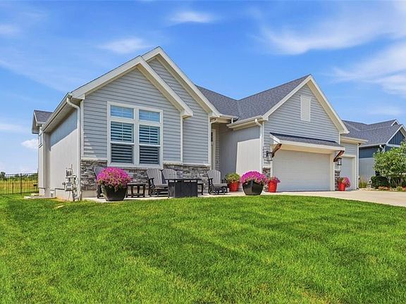 Exterior featuring light gray siding, stone accents, two-car garage, front patio, and a fenced yard
