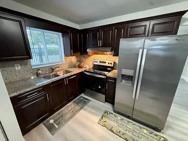 Kitchen with Large Stainless Steel Refrigerator and Glass Top Stove with Oven. Kitchen has Granite Countertop and Backsplash