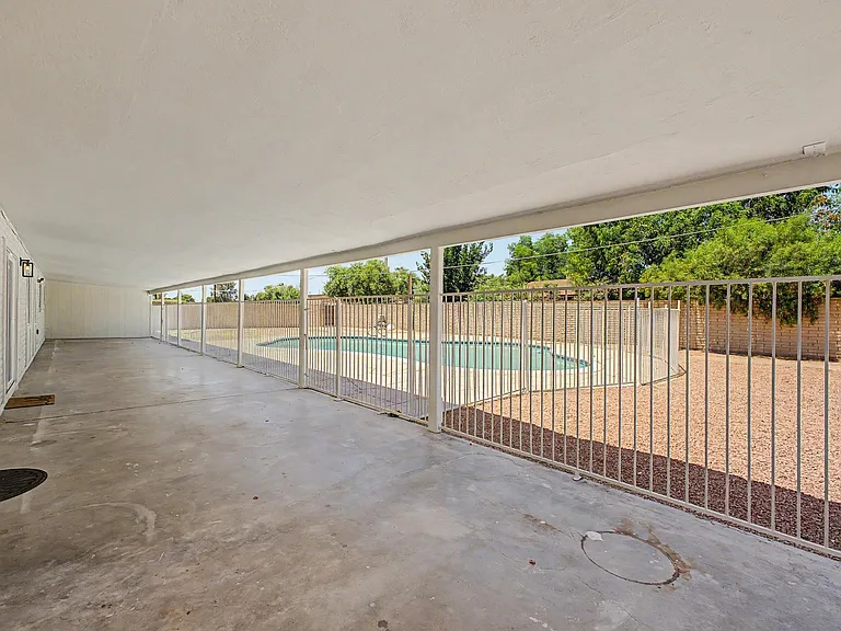 Covered rear patio with a large concrete slab and security railing, overlooking a fenced backyard pool area.