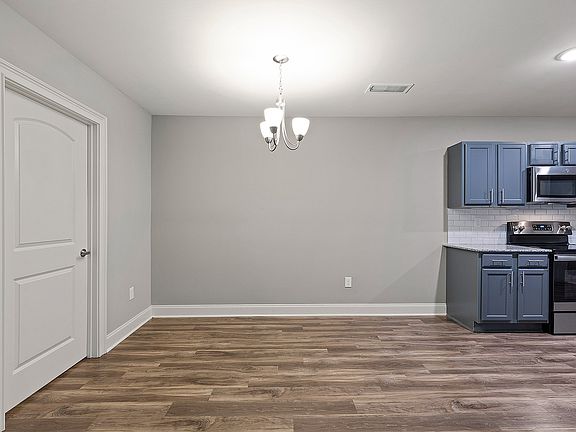 Modern kitchen & dining space with sleek gray cabinetry and stainless steel appliances, complemented by elegant wood flooring and a stylish overhead chandelier.