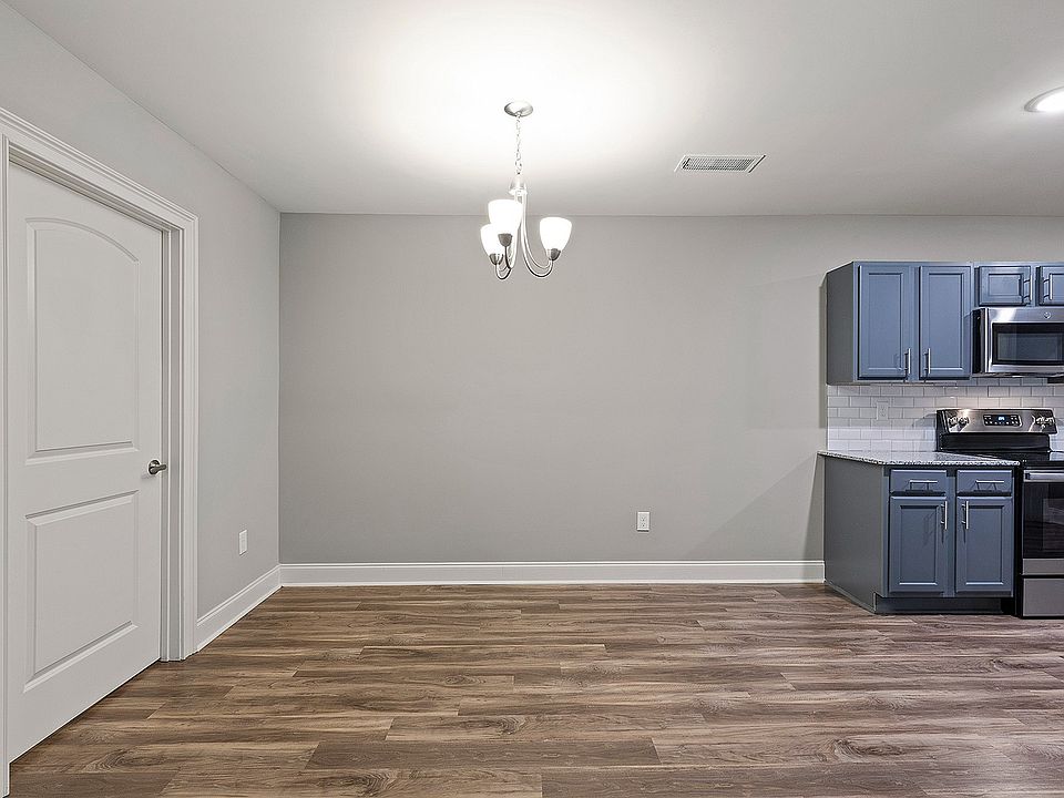 Modern kitchen & dining space with sleek gray cabinetry and stainless steel appliances, complemented by elegant wood flooring and a stylish overhead chandelier.