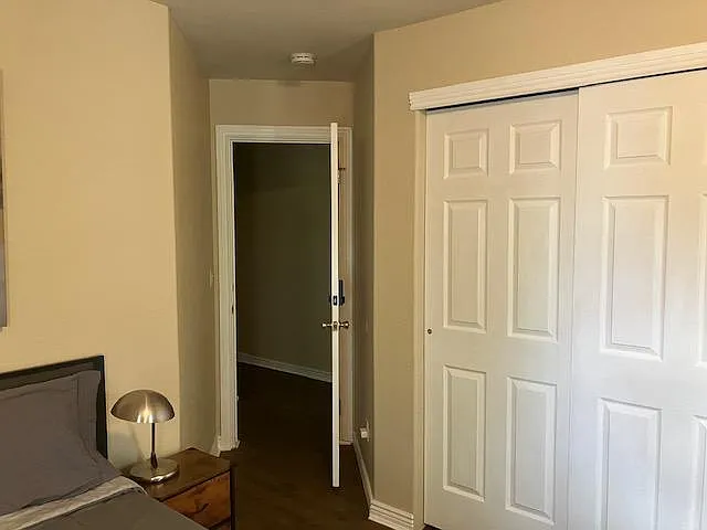 Bedroom with sliding-door closet, nightstand lighting, and easy access to the hallway for convenient daily routines.