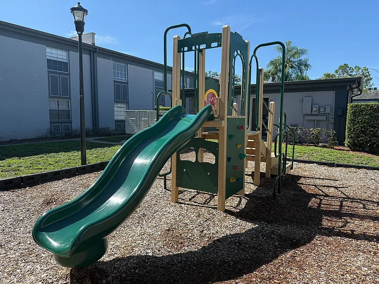Inviting outdoor playground with a vibrant green slide and climbing area, perfect for children's play in a sunny apartment community.