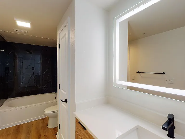 Apartment bathroom with large soaking tub, wood-style flooring and LED vanity mirror.