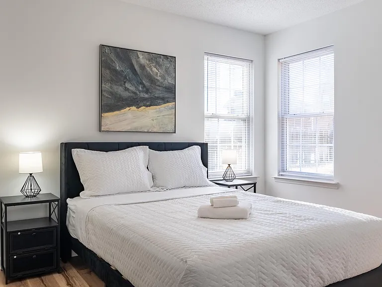 Well-appointed bedroom with a queen bed, nightstands, and two windows with blinds for plenty of natural light.