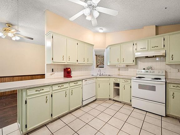 Kitchen with white appliances, under cabinet range hood, a ceiling fan, a peninsula, and a textured ceiling