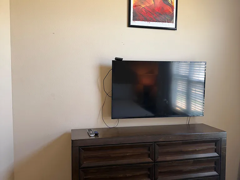 Furnished bedroom featuring a dresser with mounted TV and wall art, offering convenient storage and in-room entertainment.