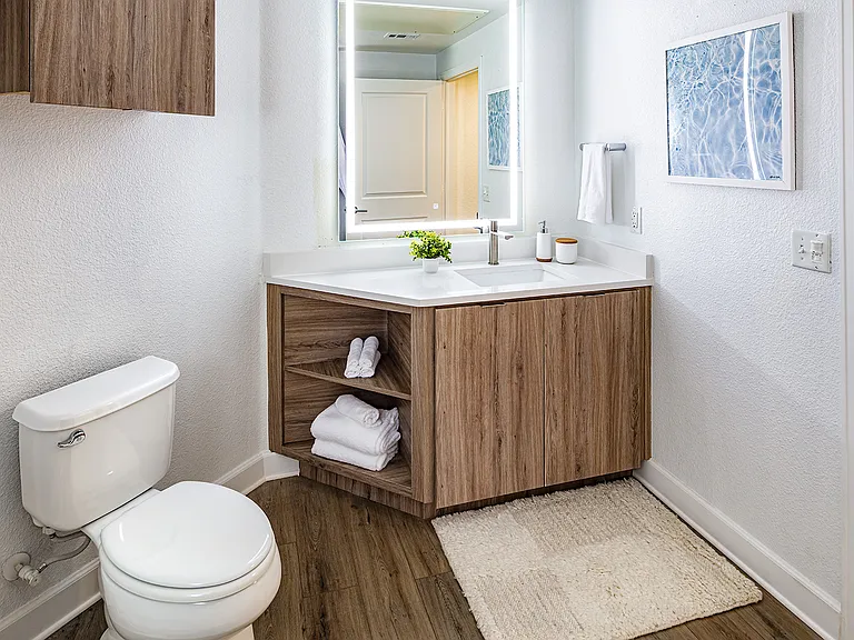 A bathroom with a wood vanity, an illuminated mirror, and a toilet next to a shower/tub combo