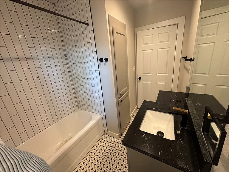 Bathroom featuring a bathtub with subway tile surround, patterned floor tiling, and a dark stone-finish countertop with an undermount sink
