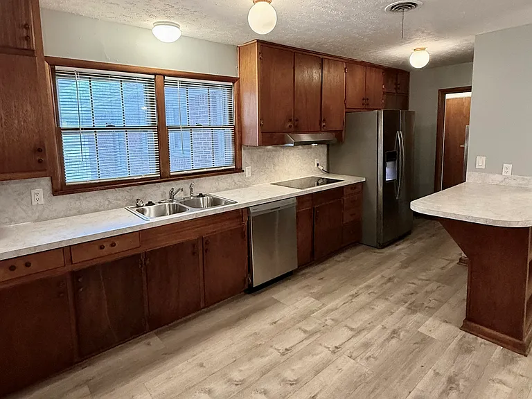 The kitchen counter, sink and dishwasher, stove and new vent hood looking towards the main hallway. The windows face the backyard.