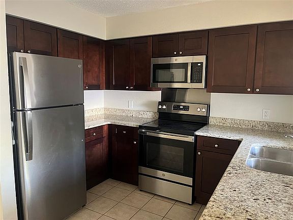 Kitchen featuring a textured ceiling, light countertops, appliances with stainless steel finishes, a sink, and light tile patterned floors