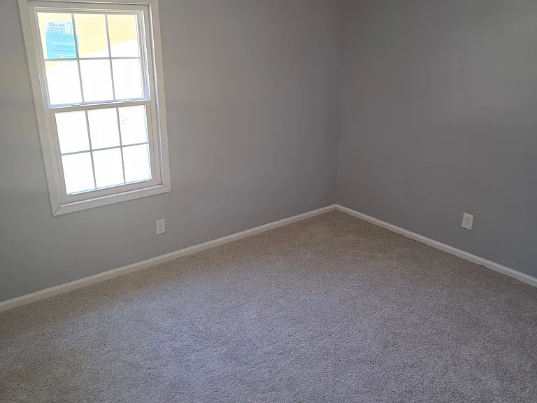 Enjoy a comfortable and peaceful bedroom featuring plush carpeting, modern gray walls, and a large window that provides plenty of natural light. The neutral finishes create a warm and inviting atmosphere while offering a versatile space that can easily ac