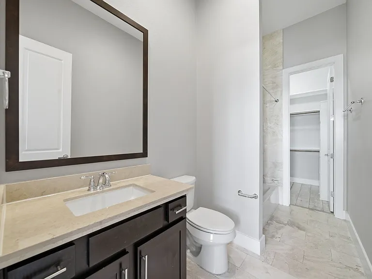 Modern downstairs ensuite bathroom featuring a sleek vanity with an oversized mirror, neutral tile flooring, and a private toilet. The adjacent walk-in shower showcases elegant marble accents, creating a clean atmosphere with spacious, contemporary feel.