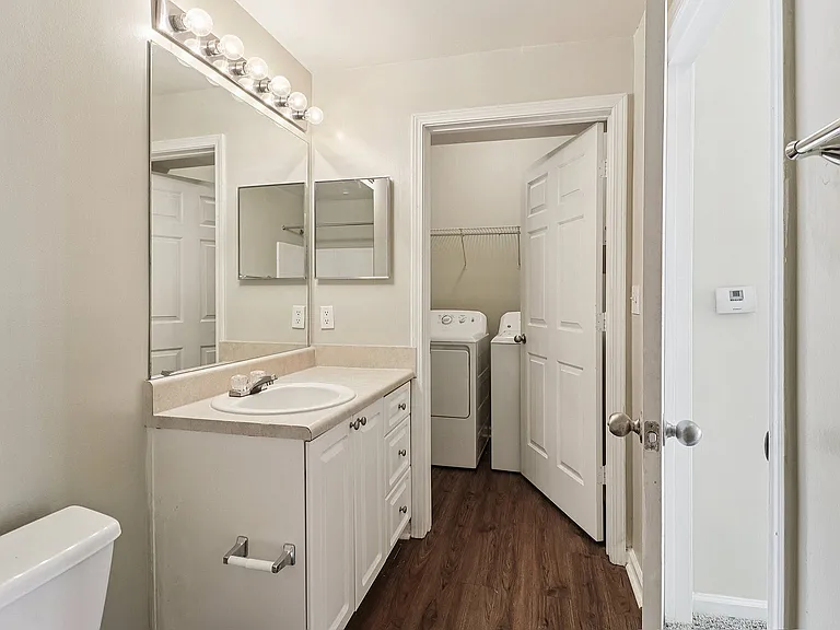 Elegant bathroom featuring a wide mirror, sleek vanity, and convenient in-unit laundry area with washer and dryer.