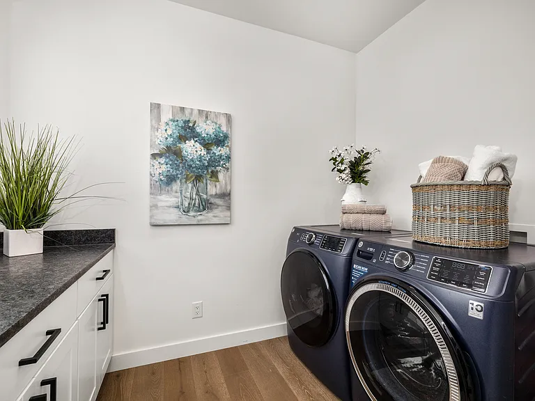 Dedicated second-floor laundry room designed for everyday Montana living, featuring scenic window views, a long countertop with generous built-in storage, and a spacious, functional layout with washer and dryer included.